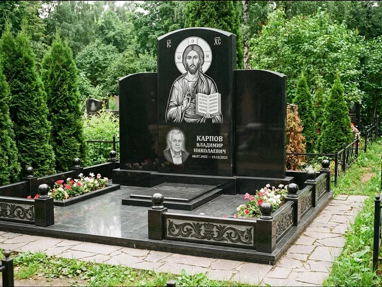 Памятник с гравировкой иконы: широкая панорамная стела с золочёным нимбом — гравировка образа Матроны Московской, цветник с белыми хризантемами, работа «Мельникова» в Хабаровске