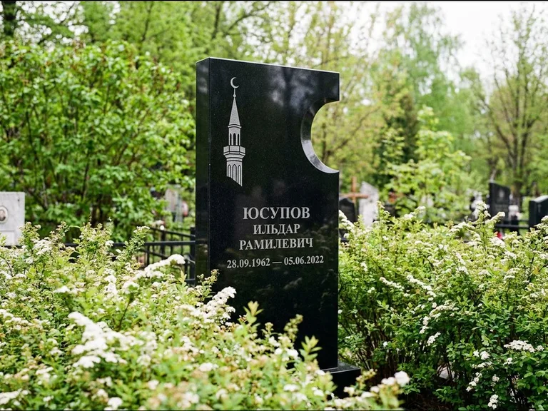 Мусульманский памятник с гравировкой мечети: стела с боковым вырезом в форме полумесяца — гравировка минарета с полумесяцем, низкие кусты спиреи в цвету, работа «Юсупов» в Хабаровске
